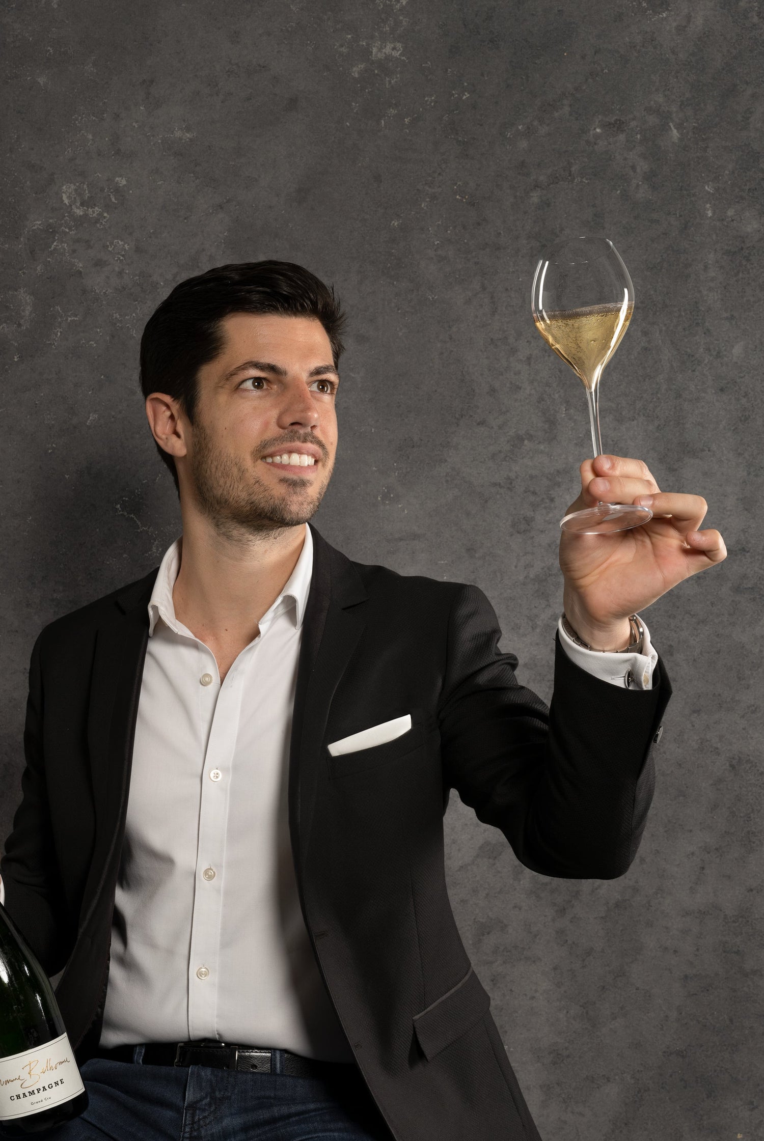 Man in a suit holding a bottle of champagne and a glass against a dark background