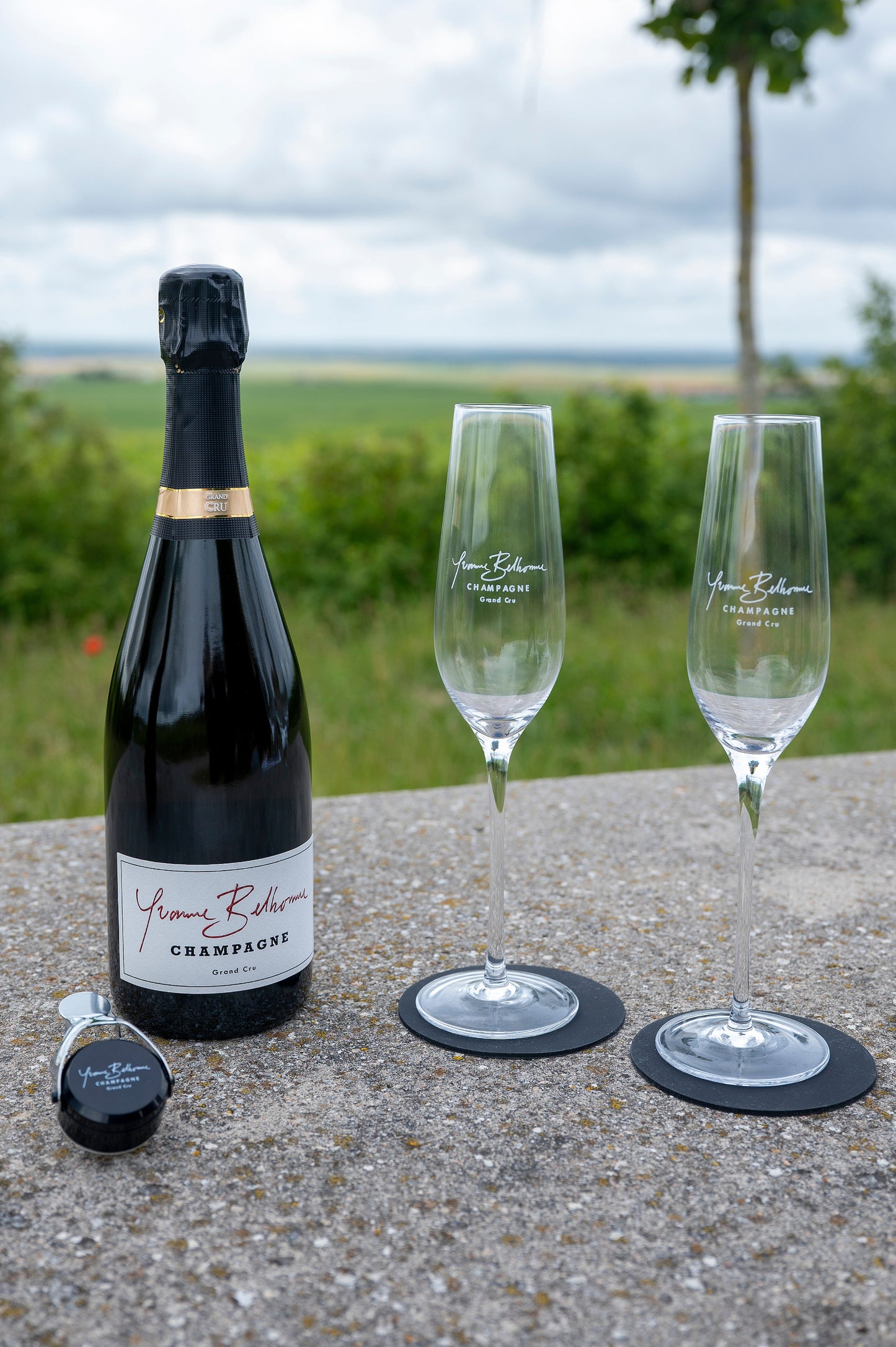 Bottle of Yvonne Belhomme champagne and two flutes on a table with a scenic background