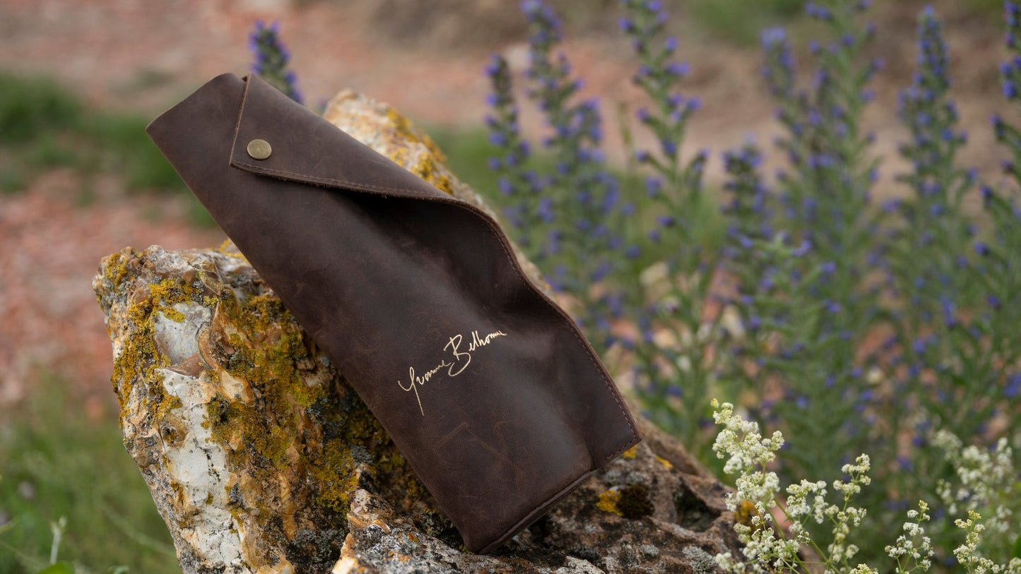 Brown leather pouch with Yvonne Belhomme branding on a rock with flowers in the background