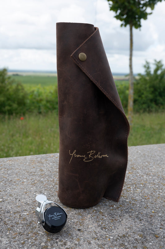 Bottle stopper and Brown leather bottle cover with 'Yvonne Belhomme' branding on a stone surface with a natural background.