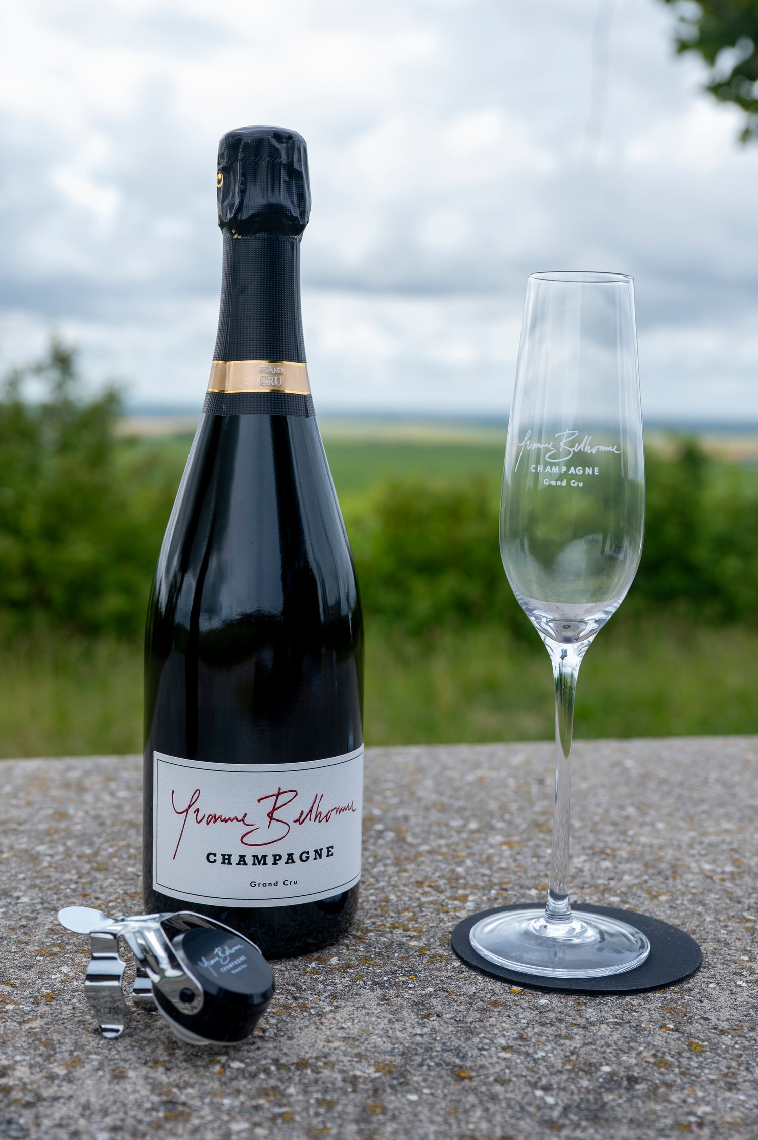 Bottle of champagne Yvonne Belhomme with a glass on a table outdoors and a bottle stopper