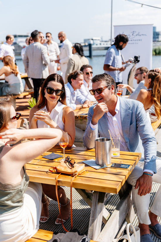 People enjoying a meal and drinks champagne outdoors by a waterfront.