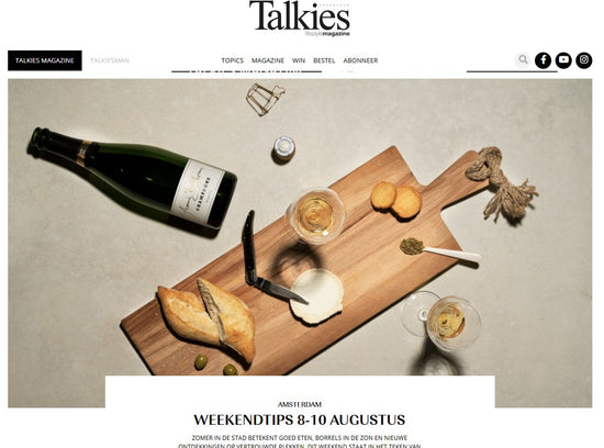 Bottle of champagne, wooden cutting board with food, and glasses on a neutral background with 'Talkies' branding.