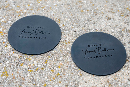 Two black coasters with 'Yonne Belhomme Champagne' text on a stone surface.