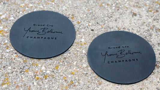 Two black coasters with 'Yonne Belhomme Champagne' text on a stone surface.