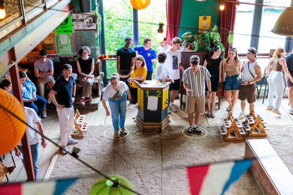A group of people playing a board game in a rustic, decorated indoor space with string lights, lanterns, and bunting flags.